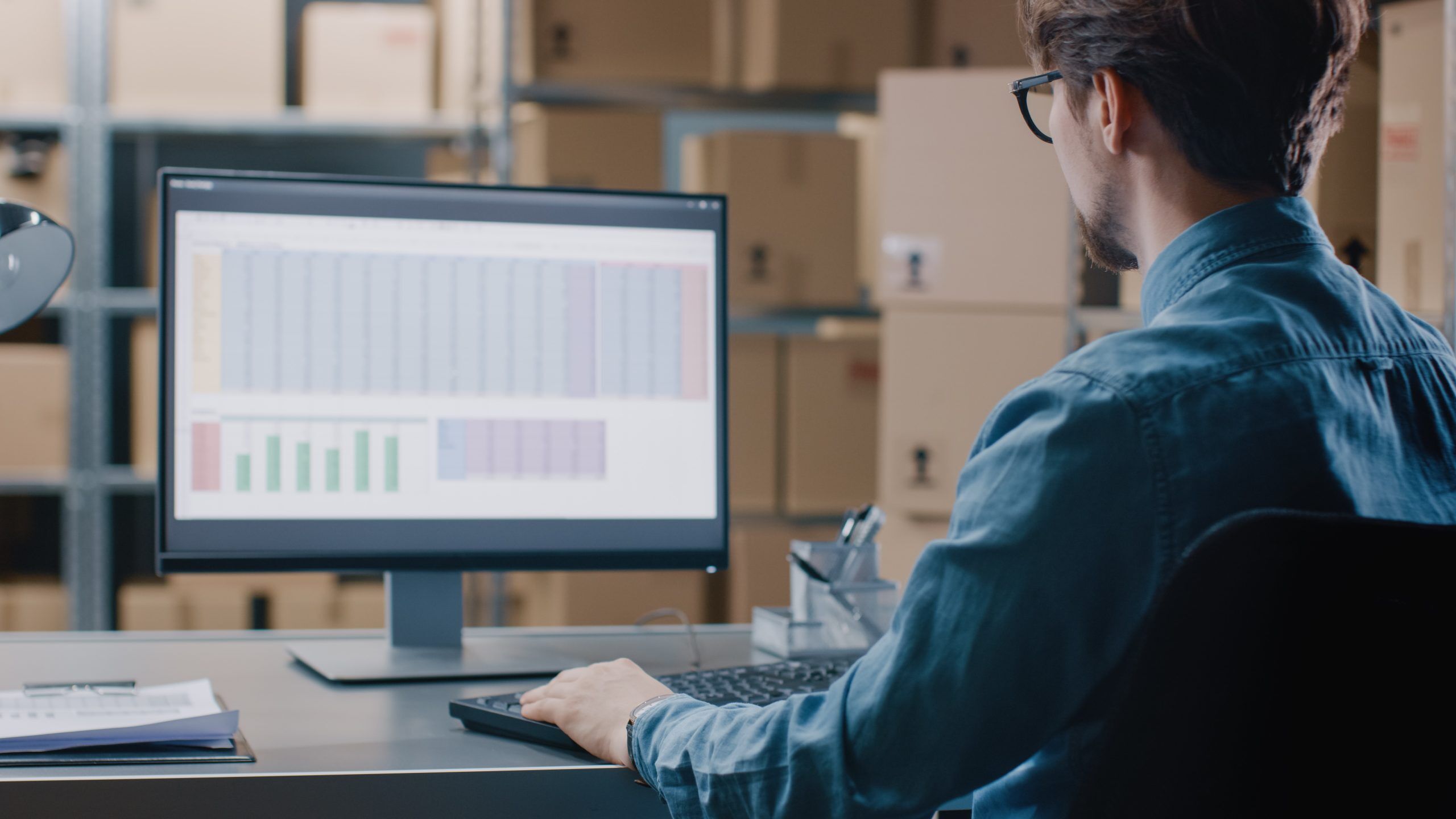 A side image of a man working on spreadsheets on his computer monitor