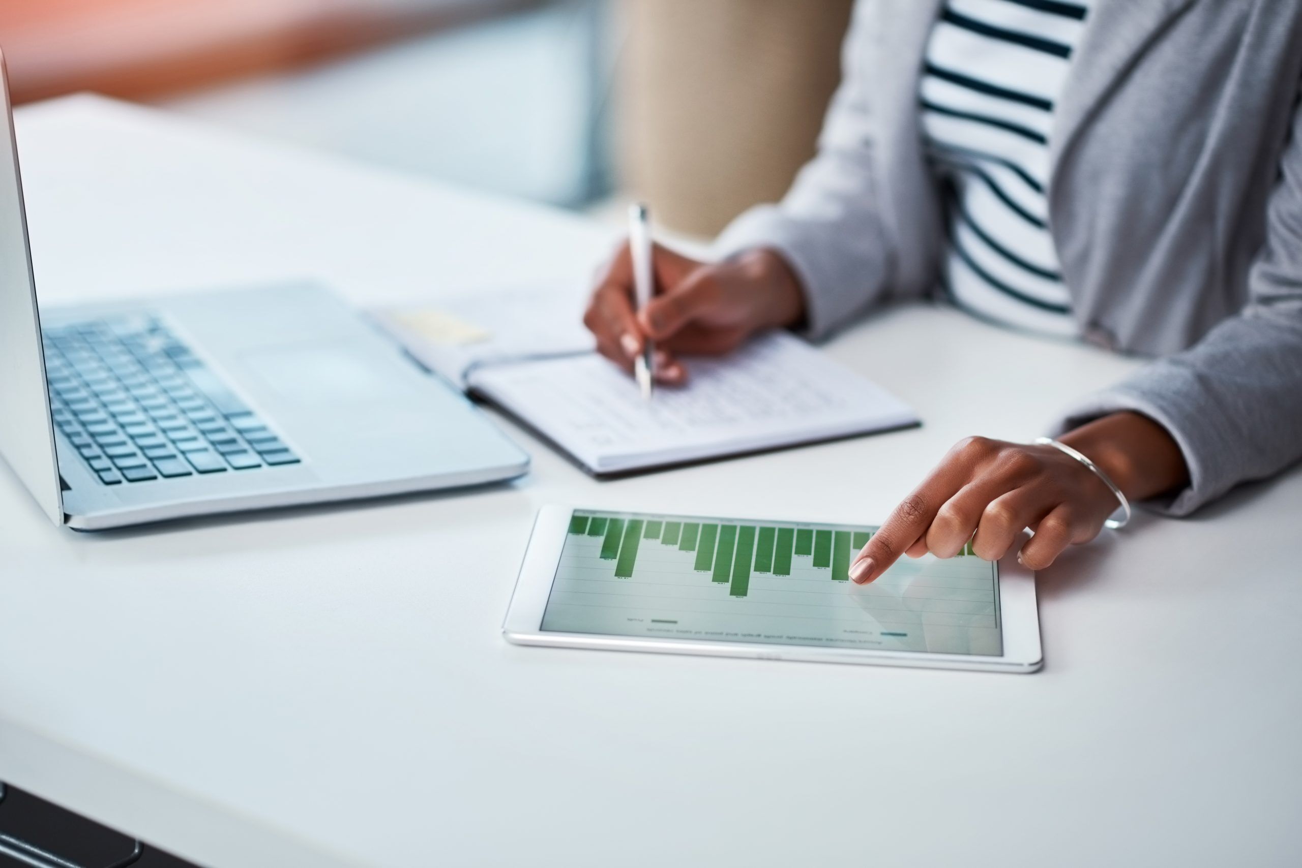 A photo of a pair of female hands while she works on a tablet and takes notes in a notebook