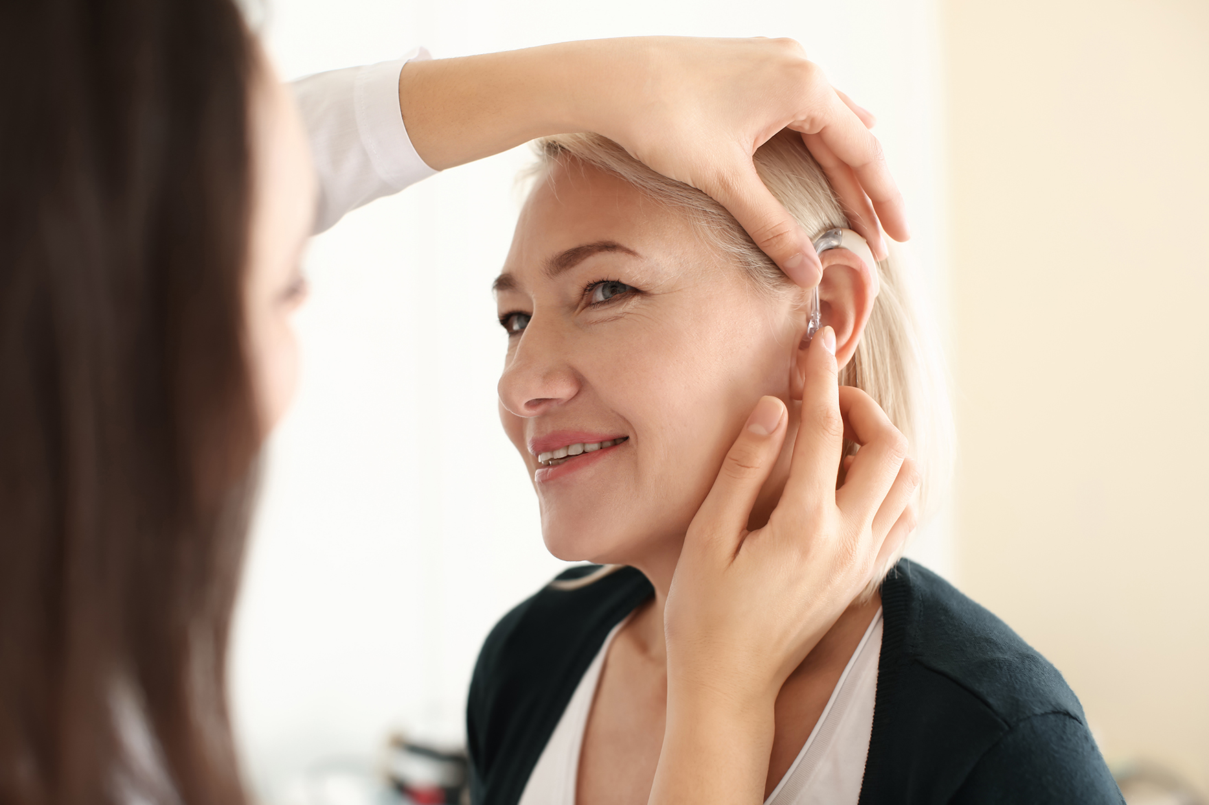 Audiologist putting hearing aid in woman's ear